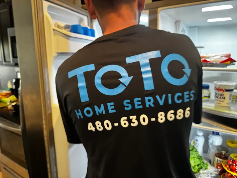 A person wearing a TOTO Home Services shirt with a phone number stands in front of an open refrigerator.