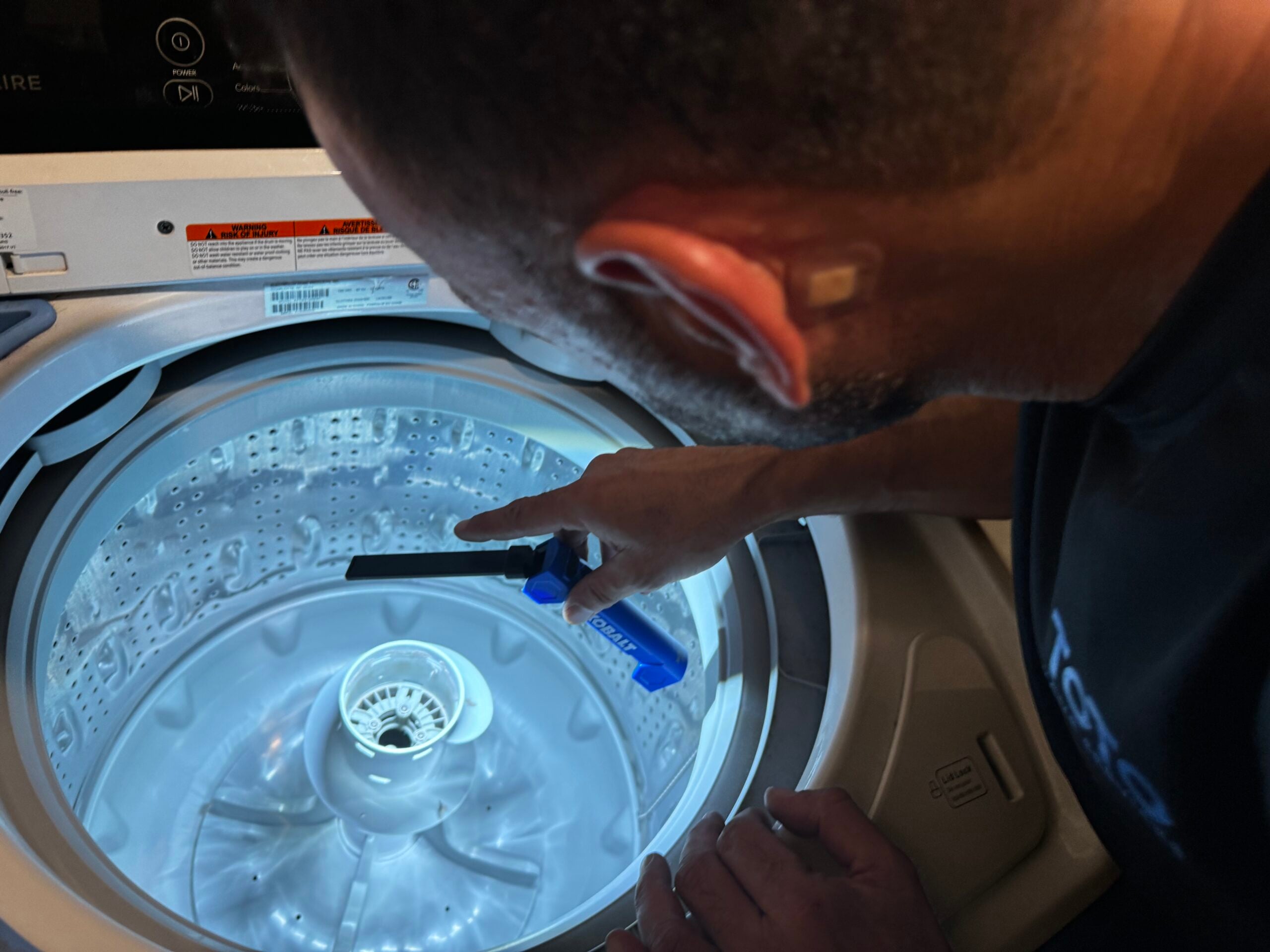 birthday-party-01 A person uses a blue cleaning brush to scrub the inside of a top-loading washing machine.