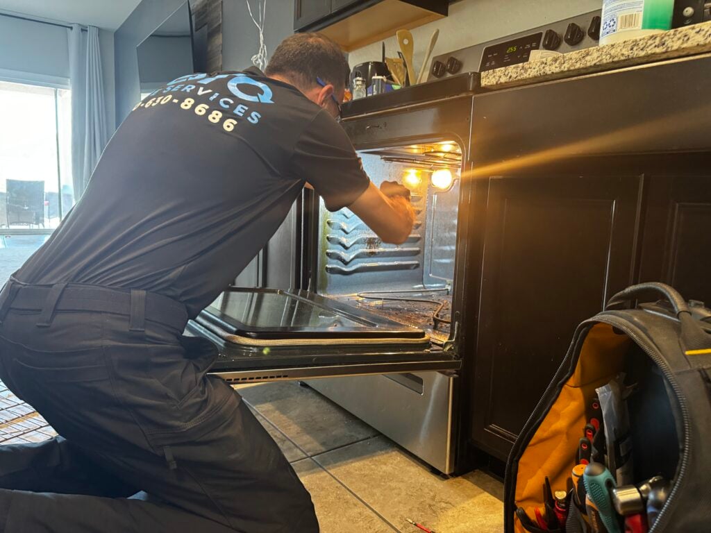 A technician kneels in front of an open oven, inspecting the interior with tools and a tool bag nearby on the kitchen floor. A technician kneels in front of an open oven, inspecting the interior with tools and a tool bag nearby on the kitchen floor.