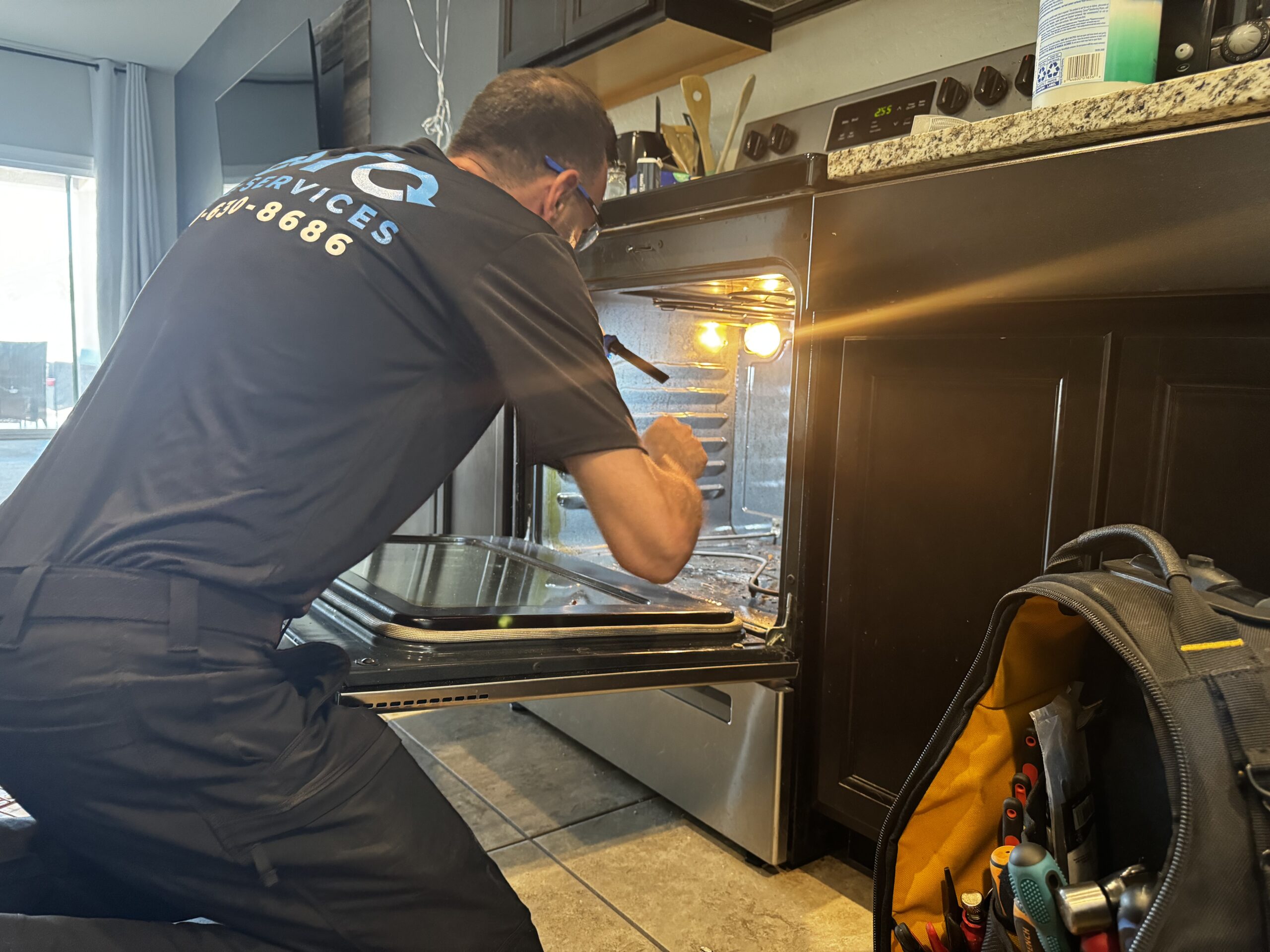 Oven Broiler Not Working — Is It the Element, the Igniter, or Something in the Control Board? A TOTO Appliance Repair technician in a black uniform inspects the interior of a built-in wall oven in a modern kitchen with a tool bag nearby.
